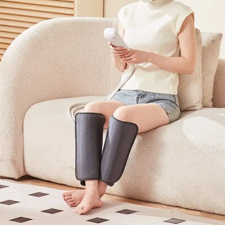 User sitting on a couch wearing RelaxRiser™ LegEase Pro heated air compression calf massager with handheld controller during relaxation